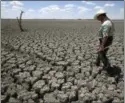  ?? AP PHOTO/TONY GUTIERREZ, FILE ?? In this Aug. 3, 2011 file photo, Texas State Park police officer Thomas Bigham walks across the cracked lake bed of O.C. Fisher Lake, in San Angelo, Texas. The impacts of record-breaking heat and years of low or no rainfall can be felt years after a dry spell passes.