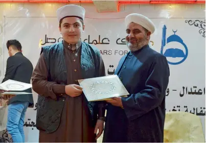 ?? AFP ?? Sheikh Saleh Al Obeidi, head of the Scholars Forum of Mosul, hands out a certificat­e to a new graduate during a graduation ceremony in the northern Iraqi city. —