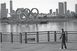  ?? EUGENE HOSHIKO/AP ?? A man wearing a protective mask to help curb the spread of COVID-19 walks near the Olympic rings floating in the water in the Odaiba section in Tokyo on Jan. 20.