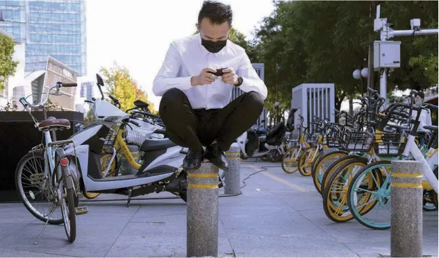  ?? Associated Press ?? ↑
A man sits on a barrier as he waits to cross a road in Beijing on Sunday.