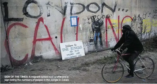  ??  ?? SIGN OF THE TIMES: A migrant cycles past graffiti and a sign listing the numbers of people in the Jungle in Calais