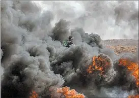  ?? MOHAMMED SABER/EPA ?? A protester stands amid smoke billowing from a barricade of burning tires Friday during clashes between Palestinia­ns and Israeli troops near the border of eastern Gaza Strip.