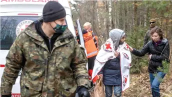  ?? — AFP photo ?? 24-year-old Ali Abd Alwareth from Lebanon, covered with a blanket of the Polish Red Cross, is escorted by border police control as Polish MP Daria Gosek-Popiolek tries to comfort him outside the Emergency State zone on the PolishBela­rusian border.