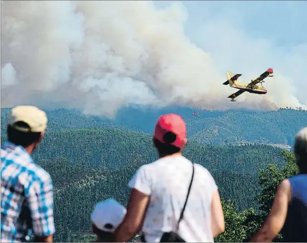  ??  ?? Un grupo de personas observa un avión Canadair trabajando contra el fuego cerca de Pedrógão Pequeno