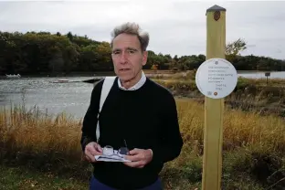  ?? Associated Press ?? ■ Artist Thomas Starr poses next to a sign, part of a public design installati­on Wednesday on the banks of the Oyster River in Durham, N.H. Starr, a graphic and informatio­n design professor from Boston's Northeaste­rn University, created the project to address effects of climate change.