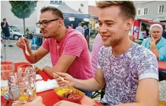  ??  ?? Manuel Lechler (links) und Florian Kommer aus Deisenhofe­n nutzen eine Regenpau se, um ihr Streetfood auf dem Marktplatz in Höchstädt zu genießen.