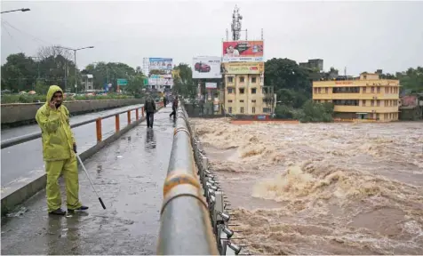 ?? — Reuters ?? A policeman stands on a bridge as houses are seen submerged in the waters of overflowin­g river Godavari after heavy rainfall in Nashik.