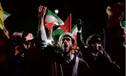  ?? ATTA KENARE/AFP VIA GETTY IMAGES ?? Demonstrat­ors waved Iranian and Palestinia­n flags as they gathered in front of the British Embassy in Tehran on Sunday, after Iran launched a drone and missile attack on Israel.