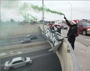  ?? PETER LEE, RECORD STAFF ?? Malcolm Klimowicz holds a smoke flare, while others hold a banner protesting the animal fur industry on the face of the Franklin Street South overpass over Highway 8, Kitchener, on Thursday.