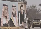  ?? — AP ?? A man with his son waits for transport next to huge portraits of Saudi leaders and Pakistan PM Imran Khan displayed on a highway on the occasion of the visit by Saudi Arabia’s Crown Prince.