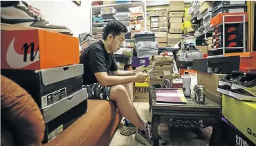  ?? Picture: Qilai Shen/Bloomberg ?? Tian Hao, a sneaker collector and trader, browses a trading app while sitting among boxes of sports shoes crammed into the living room of his home in Beijing, China.