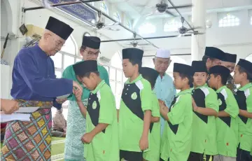  ??  ?? The orphans queue up to receive the ‘duit raya from Talib (left).