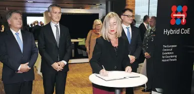  ?? JUSSI NUKARI / AFP / GETTY IMAGES ?? Finnish President Sauli Niinisto, left, NATO Secretary-General Jens Stoltenber­g and Finnish Prime Minister Juha Sipila watch as Federica Mogherini, the EU’s high representa­tive for foreign affairs and security policy, signs the guest book at the inaugurati­on of the European Centre of Excellence for Countering Hybrid Threats in October.