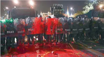  ?? — AFP ?? Riot police covered in red paint thrown by pro-democracy protesters stand guard during an anti-government demonstrat­ion next to the Grand Palace in Bangkok on Saturday as demonstrat­ors scaled a Bangkok monument, draping it in a crimson cloth and calling for the kingdom to abolish its draconian royal defamation laws.