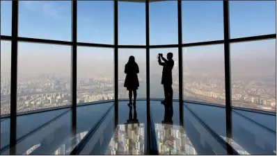  ?? Bloomberg News/SEONGJOON CHO ?? Visitors are silhouette­d as they take photograph­s from the glass-bottomed observatio­n deck at the Lotte Corp. World Tower in Seoul, South Korea, earlier this month.