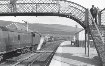  ?? Roy Hobbs/Transport Treasury ?? A view from the down platform records the Inverness-bound train on arrival, the 4-6-0 just ahead of the staff-only wooden footboards betwixt platforms. The full brake is a 50ft steel-sided LMS variant, 8ft 6in wide and the maximum 9ft across the centrally-placed guard’s duckets. The guard had a seat beside these and may find himself surrounded by mail and parcels, the van being open plan, so its use is perhaps surprising given that mail was being carried and that passengers passed through the vehicle when it was marshalled in the middle of a train with a restaurant car, as would soon be the case here. Perhaps the lingering pedestrian on the lattice footbridge is Hugh Davies, who went on to photograph much of the shunt from that position. Meanwhile, a member of the station staff crosses to the down platform in readiness for the impending arrival of the 10.30am Inverness to Kyle of Lochalsh service.