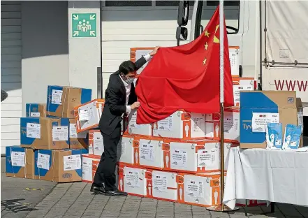  ?? AP ?? A man arranges a Chinese flag in front of boxes containing protective suits and masks in Vienna yesterday. China has donated 3000 protective suits and 150,000 masks to emergency organisati­ons in Austria, as infections in China decline and Europe becomes the epicentre of the global coronaviru­s pandemic.