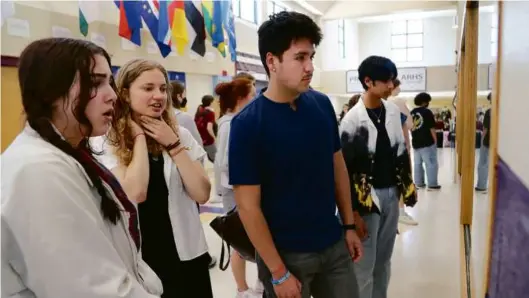  ?? JOHN TLUMACKI/GLOBE STAFF ?? Below, Amherst Regional High School seniors (from left) Lucia Lopez, Jane Scanlan-Emigh, and Victor Cruz-Castro looked at a trans/ nonbinary photograph­y exhibit in their school hallway in May.