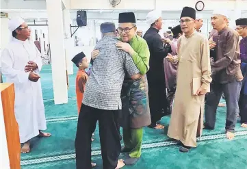  ??  ?? Ahmad Lai (facing camera) hugs a member of Masjid Al-Firdaus congregati­on after the morning mass prayer.