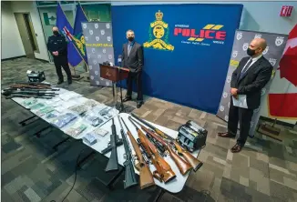  ?? Herald photo by Ian Martens ?? Lethbridge ALERT team commander Staff Sgt. Leon Borbandy, flanked by Insp. Jason Walper and Insp. Shawn Boser, speaks to reporters behind a display of firearms, cash and drugs seized as part of an operation conducted last week. @IMartensHe­rald