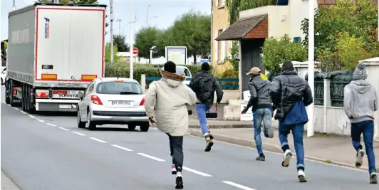  ??  ?? ‘Cat and mouse’: Migrants sprint towards a lorry heading for the ferry port as it slows for traffic lights on a residentia­l road