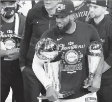  ?? MIKE EHRMANN/GETTY ?? LeBron James holds the NBA Finals and Finals MVP trophies Sunday night.