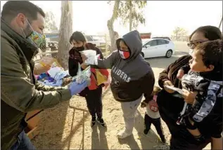  ??  ?? CASTORENA, left, gives masks to community members at a weekly food giveaway, where he also plays music to lif t spirits. “Every day, I feel like I can help the kid my dad used to be,” he said.