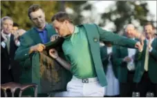  ?? CHRIS CARLSON — THE ASSOCIATED PRESS ?? Defending champion Jordan Spieth, left, helps 2016 Masters champion Danny Willett, of England, put on his green jacket following the final round of the Masters golf tournament Sunday in Augusta, Ga.