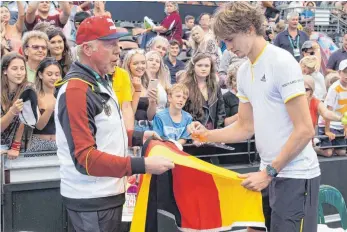  ?? FOTO: DPA ?? Die Legende als Helfer: Boris Becker (li.) hält Alexander Zverev eine Fahne hin, auf die der 20-Jährige unterschre­iben soll.