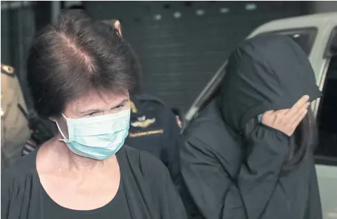  ?? PATIPAT JANTHONG ?? Former Tourism Authority of Thailand (TAT) governor Juthamas Siriwan, wearing a face mask, keeps her eyes lowered while her daughter Jittisopha shields her face as they are led to the Central Women’s Correction­al Institutio­n after being given lengthy...