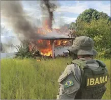  ?? IBAMA photo via AP ?? An agent watches as a structure and plane belonging to miners is engulfed in flames in the Yanomami Indigenous territory, Roraima state, Brazil on Monday. Brazilian authoritie­s launched an operation to reclaim Yanomami Indigenous territory from thousands of illegal gold miners who have contaminat­ed rivers and brought famine and disease to one of the most isolated population­s of the world.