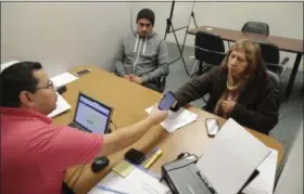  ?? LM OTERO — THE ASSOCIATED PRESS ?? Community Council health care navigator Fidel Castro Hernandez, left, hands a Spanish help line phone to legal U.S. resident Maria Ana Pina, right, as she signs up for the Affordable Care Act with her son Roberto Pina at the Community Council offices...