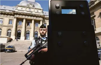  ?? Francois Mori / Associated Press ?? A police officer stands behind a shield outside the Paris courthouse where 20 men are accused of Islamic State terror attacks in 2015 that killed 130 people and injured hundreds more.