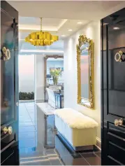  ??  ?? Glossy black doors open to a sophistica­ted foyer set off by a gold light fixture and furry, white bench.