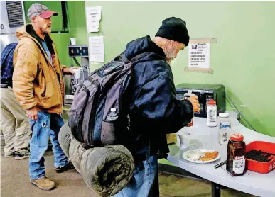  ?? [PHOTOS BY JIM BECKEL, THE OKLAHOMAN] ?? Wearing a backpack and carrying his bedroll, this man whose street name is “Stranger” prepares his breakfast plate at the Homeless Alliance’s day shelter on NW 3 Street on Oct. 19.