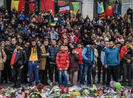  ?? DANIEL BEREHULAK/THE NEW YORK TIMES ?? Surrounded by flags, people pay tribute to victims of the Brussels attacks during a moment of silence at Place de la Bourse, in Brussels, on Thursday.