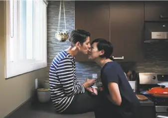  ?? Gabrielle Lurie / The Chronicle ?? Courtney Howard (left) kisses wife Ingrid Hu Dahl as they make dinner in San Francisco. The two are planning a personal foundation to fund organizati­ons fighting for gender equality.