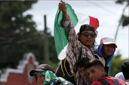  ?? MOISES CASTILLO — THE ASSOCIATED PRESS ?? Central American migrants making their way to the U.S. in a large caravan wave a Mexican flag as they arrive to Tapachula, Mexico, after a truck driver gave them a free ride, Sunday. Despite Mexican efforts to stop them at the Guatemala-Mexico border, about 5,000 Central American migrants resumed their advance toward the U.S. border Sunday in southern Mexico.