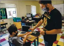  ??  ?? Teacher Omar Reynoso, right, squirts hand sanitizer on the hands of Damian Velasquez, 11.