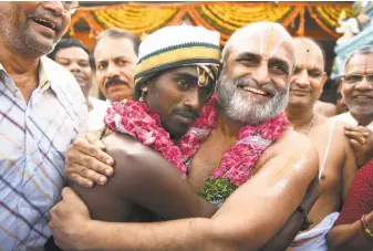  ?? Noah Seelam / AFP / Getty Images ?? C.S. Rangarajan (right) hugs Aditya Parasri during an April ritual stressing human equality. Rangarajan also serves as a priest at Chilkur Balaji Temple, where people pray for visas.