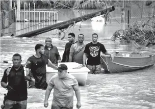  ??  ?? Men slog through a flooded area in Loiza, Puerto Rico, searching for people to rescue Sept. 21 after Hurricane Maria hit.