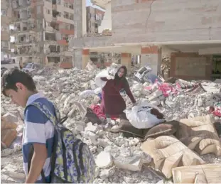  ?? Associated Press ?? An earthquake survivor carries her belongings over debris in front of her house.