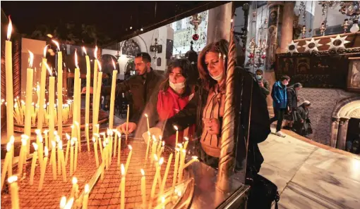  ?? ABBAS MOUMANI/AFP VIA GETTY IMAGES ?? Worshipper­s light candles at the Church of the Nativity, the traditiona­l place of Jesus’ birth, during preparatio­ns for Christmas in Bethlehem in the occupied West Bank, Dec. 19.