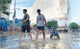  ?? AP PHOTO/DAKE KANG ?? Residents walk along a flooded road in the aftermath of the heaviest recorded rainfall in Zhengzhou in central China’s Henan province on Saturday.