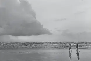  ?? Kim Brent/The Beaumont Enterprise via AP ?? n A couple strolls Saturday along the shore in McFaddin Beach, Texas, as storm clouds build on the horizon the day after Hurricane Harvey made land, battering the gulf communitie­s near Corpus Christi. Rains and wind are still expected to impact the...