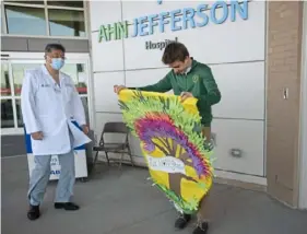  ?? Pam Panchak/Post-Gazette ?? Patrick Weldon, 14, from Carroll Township, unfurls a “Hope” banner he and his classmates made for patients at AHN Jefferson Hospital while Dr. Chong Park moves in to lend a hand.