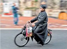  ??  ?? In full flow: a priest in a cassock rides his motorised bicycle in Lapalisse, France