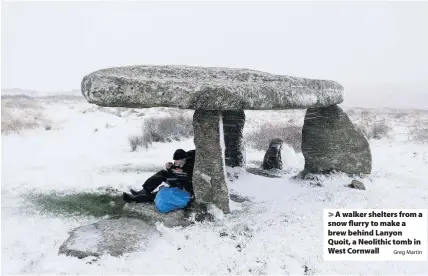  ?? Greg Martin ?? > A walker shelters from a snow flurry to make a brew behind Lanyon Quoit, a Neolithic tomb in West Cornwall