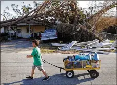  ?? DAVID GOLDMAN / AP ?? Anthony Weldon,11, pulls a cart with his family’s belongings as they relocate from their uninhabita­ble home to stay at their landlord’s place in the aftermath of Hurricane Michael in Springfiel­d, Fla., on Monday.