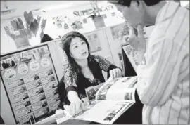  ??  ?? MAGGIE WEN explains tour packages to a customer at America Asia Travel Center, where the main effect of the China crash has been enlivened office gossip.